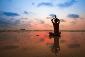 Silhouette young woman practicing yoga on the beach at sunset